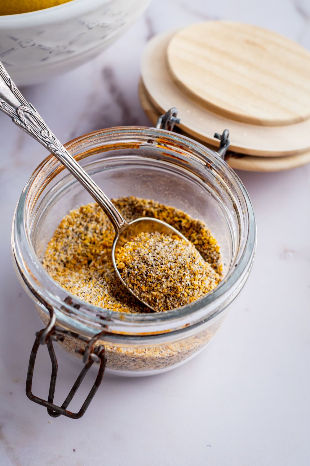 Jar of lemon pepper seasoning with a metal spoon.