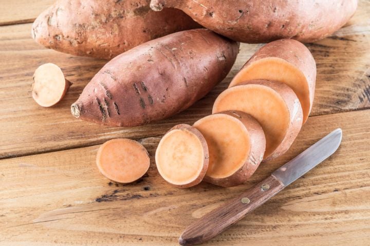 8 Reasons to Eat More Sweet Potatoes (Plus Tons of Recipe Ideas) Sweet potato on a wooden cutting board with a knife.