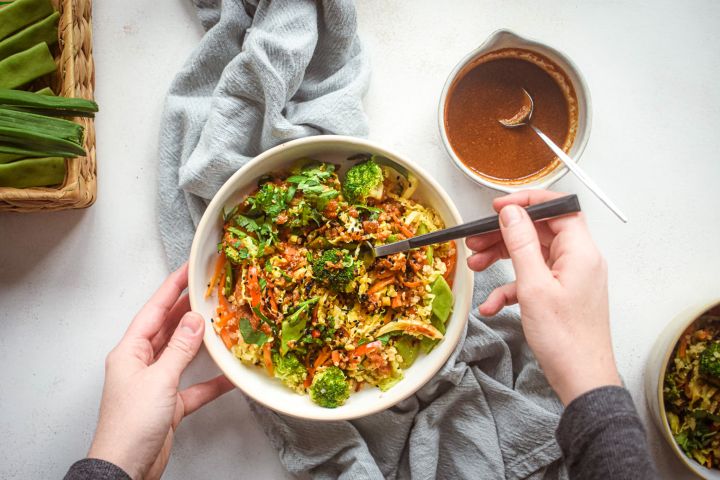 Asian Quinoa Stir Fry Asian quinoa stir fry with broccoli, carrots, cabbage, and snow peas in a bowl with stir fry sauce and sesame seeds.