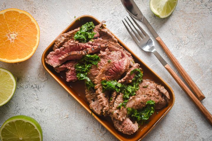 Carne Asada Carne asada marinated in citrus juices sliced thin on a plate with cilantro, limes, and orange slices.