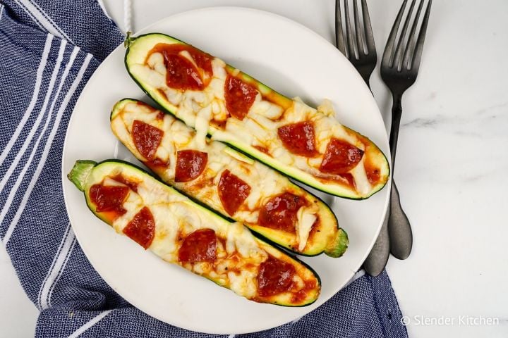 Zucchini Pizza Boats Zucchini pizza boats with marinara sauce, melted mozzarella cheese, and pepperoni on a white plate.