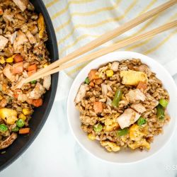 Easy Chicken Fried Rice Chicken fried rice in a bowl with eggs, peas, carrots, chicken, and green beans with chopsticks.