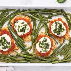 Sheet Pan Healthy Chicken Parm Healthy Chicken Parmesan with breaded chicken covered in sauce and cheese on a sheet pan with roasted green beans.