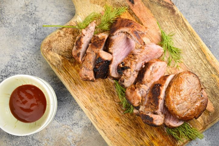 Barbecue Rubbed Pork Tenderloin Barbecue rubbed pork tenderloin sliced on a wooden board with rosemary.