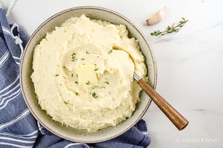 Potato Cauliflower Mash Cauliflower potato mash with roasted garlic and butter in a ceramic bowl with a wooden spoon.