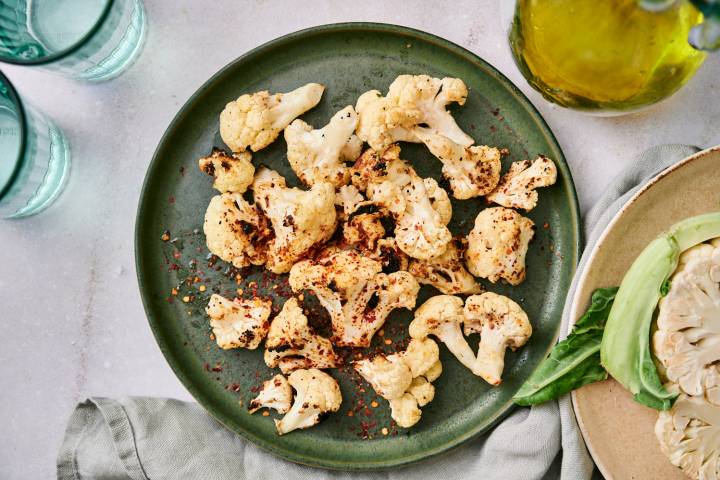 Grilled Cauliflower Grilled cauliflower with browned edges on a plate with red pepper flakes, salt, pepper, and olive oil.