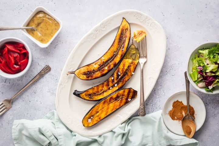 Grilled Plantains Grilled plantains with dark brown grill marks on a plate with cinnamon on the side.