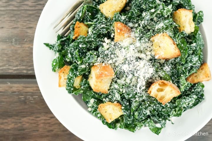 Healthy Kale Caesar Salad Kale caesar salad with croutons and Parmesan cheese on a plate with a fork.