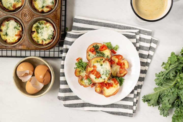 Quiche Cupcakes Quiche cupcakes with a ham crust and a cheese and spinach filling on a wire rack with cracked eggs on the side.
