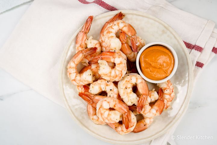 Easy Shrimp Cocktail (Roasted or Poached) Shrimp cocktail with a small bowl of sauce on a white plate.