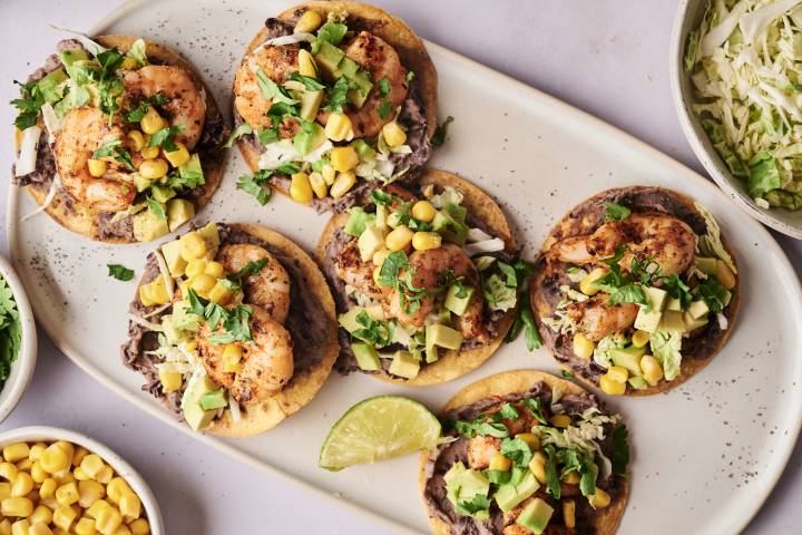 Shrimp Tostadas A plate of six shrimp tostadas with black beans, shredded cabbage, corn, avocado, and cilantro.