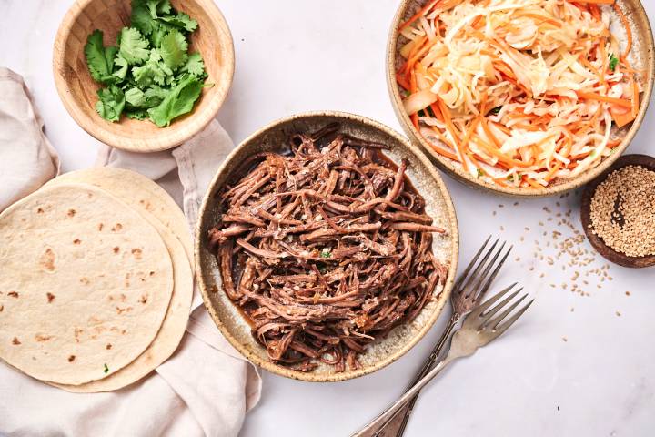 Slow Cooker Korean Beef Tacos Slow cooker Korean beef tacos with corn tortillas, coleslaw, hot sauce, and Sriracha.