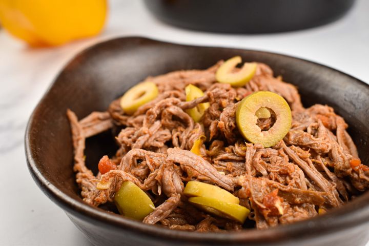 Slow Cooker Ropa Vieja Slow cooker ropa vieja with peppers, onions, tomatoes, and olives in a black dish.