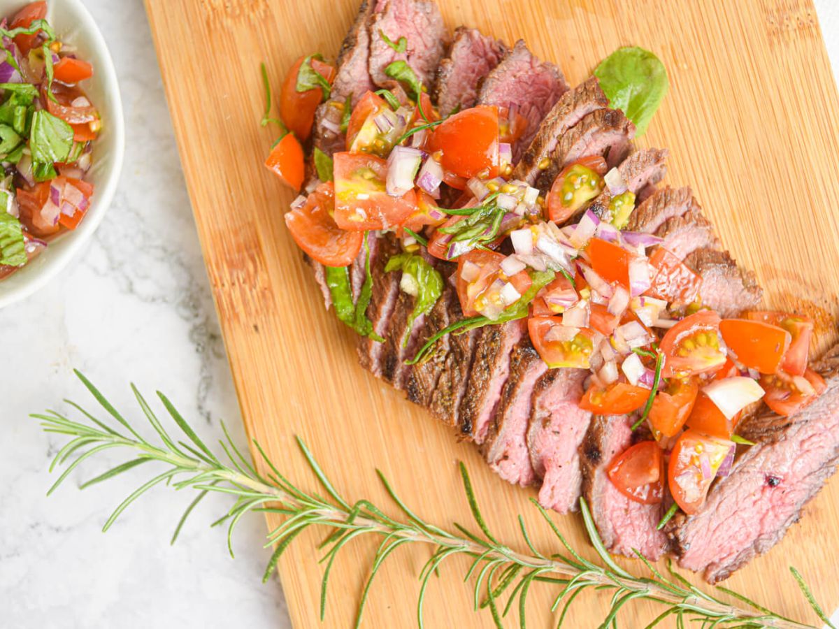Grilled Beef Grilled steak on a wooden board with tomato, and basil salad.