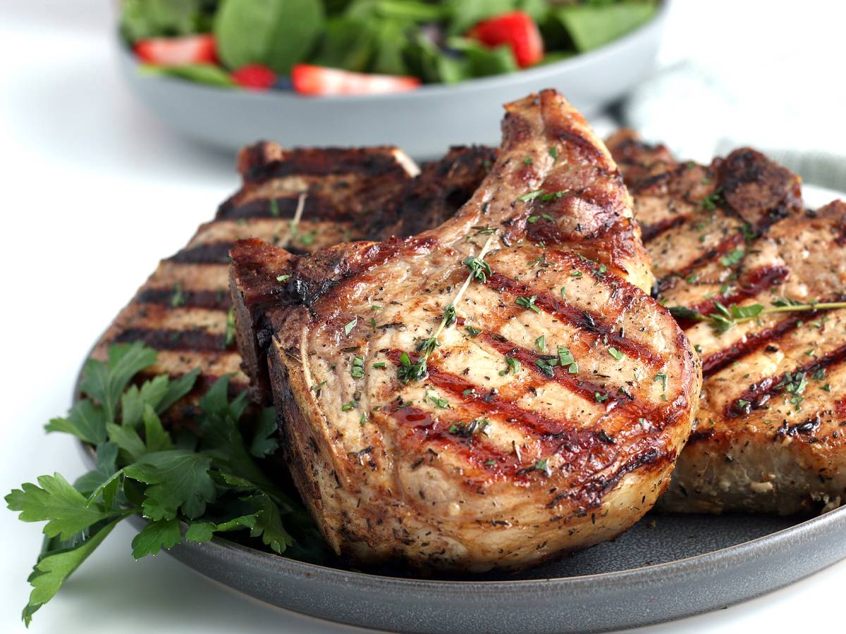 Pork Dinners Grilled pork chops with grill marks and fresh thyme on a plate.