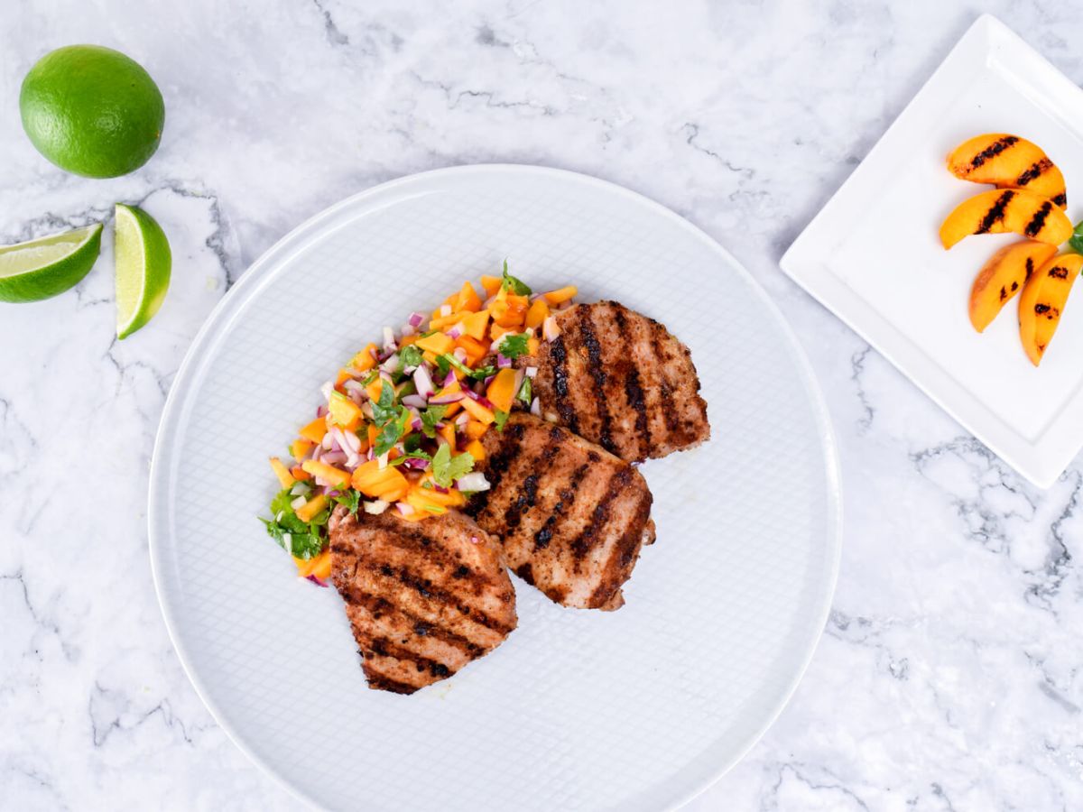 Grilled Pork White plate with grilled pork chops accompanied with peach salsa, fresh limes and peaches on the side.