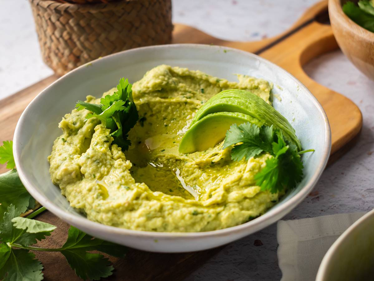 Clean Eating Avocado hummus in a bowl with cilantro and sliced fresh avocado.