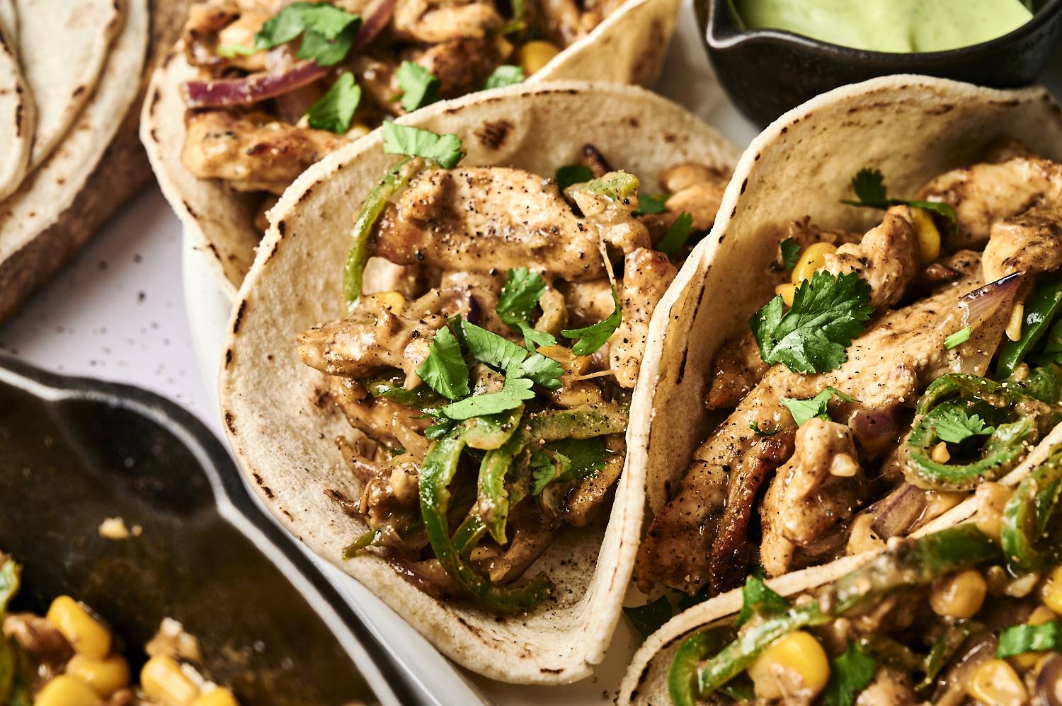 Three flavorful tacos filled with seasoned chicken, green peppers, onions, corn, and garnished with fresh cilantro, served with green sauce.