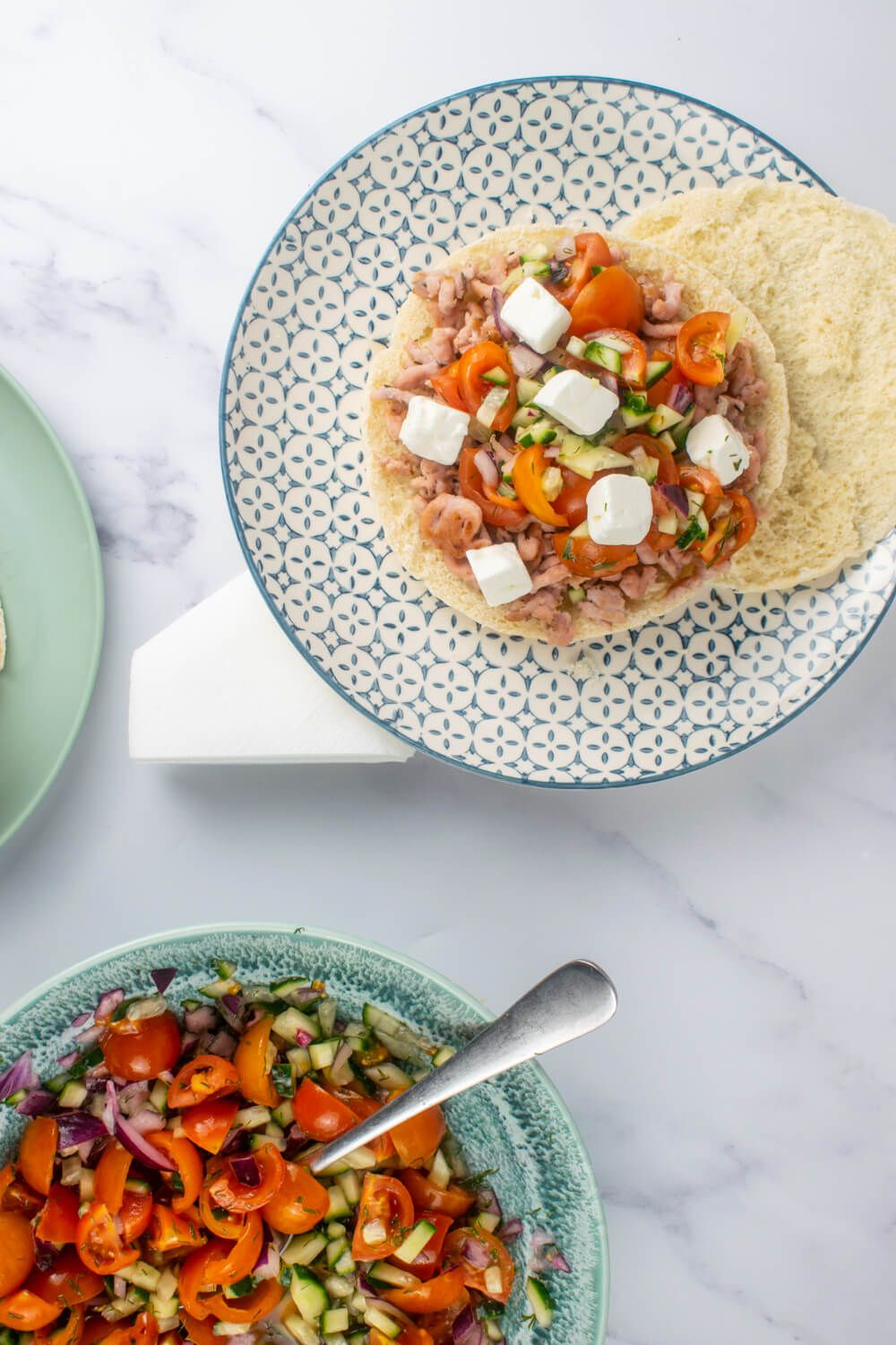 Greek tostadas with ground turkey, Greek salad, and feta cheese on a blue and white plate.