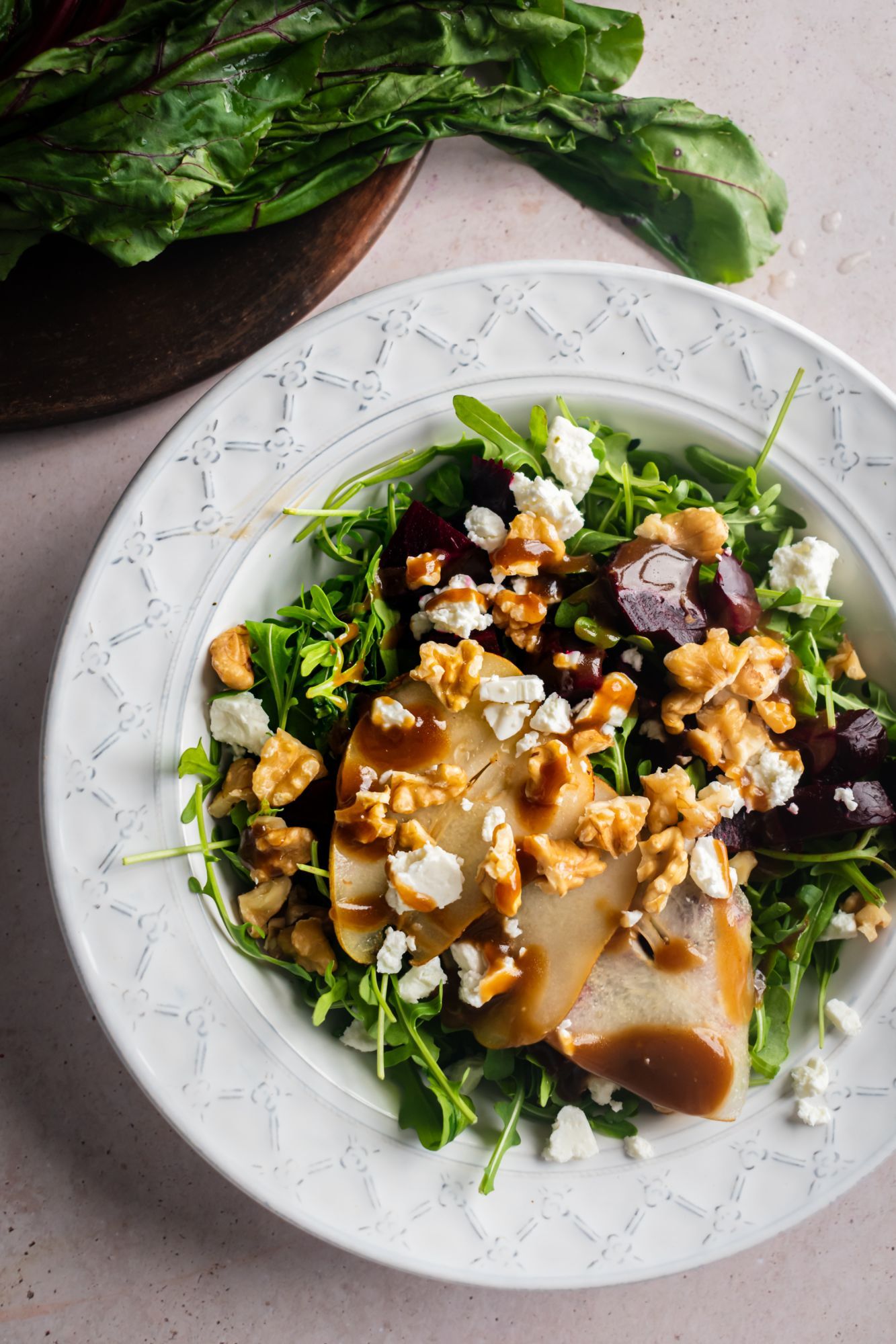 Roasted beet salad with arugula, walnuts, pears, and a balsamic dijon dressing served in a white bowl.