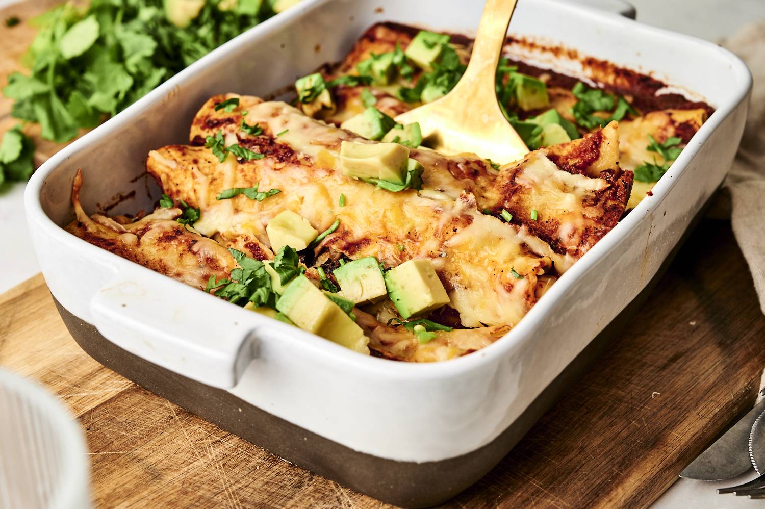 A baking dish filled with cheesy black bean enchiladas, garnished with fresh avocado chunks and cilantro, ready to be served.