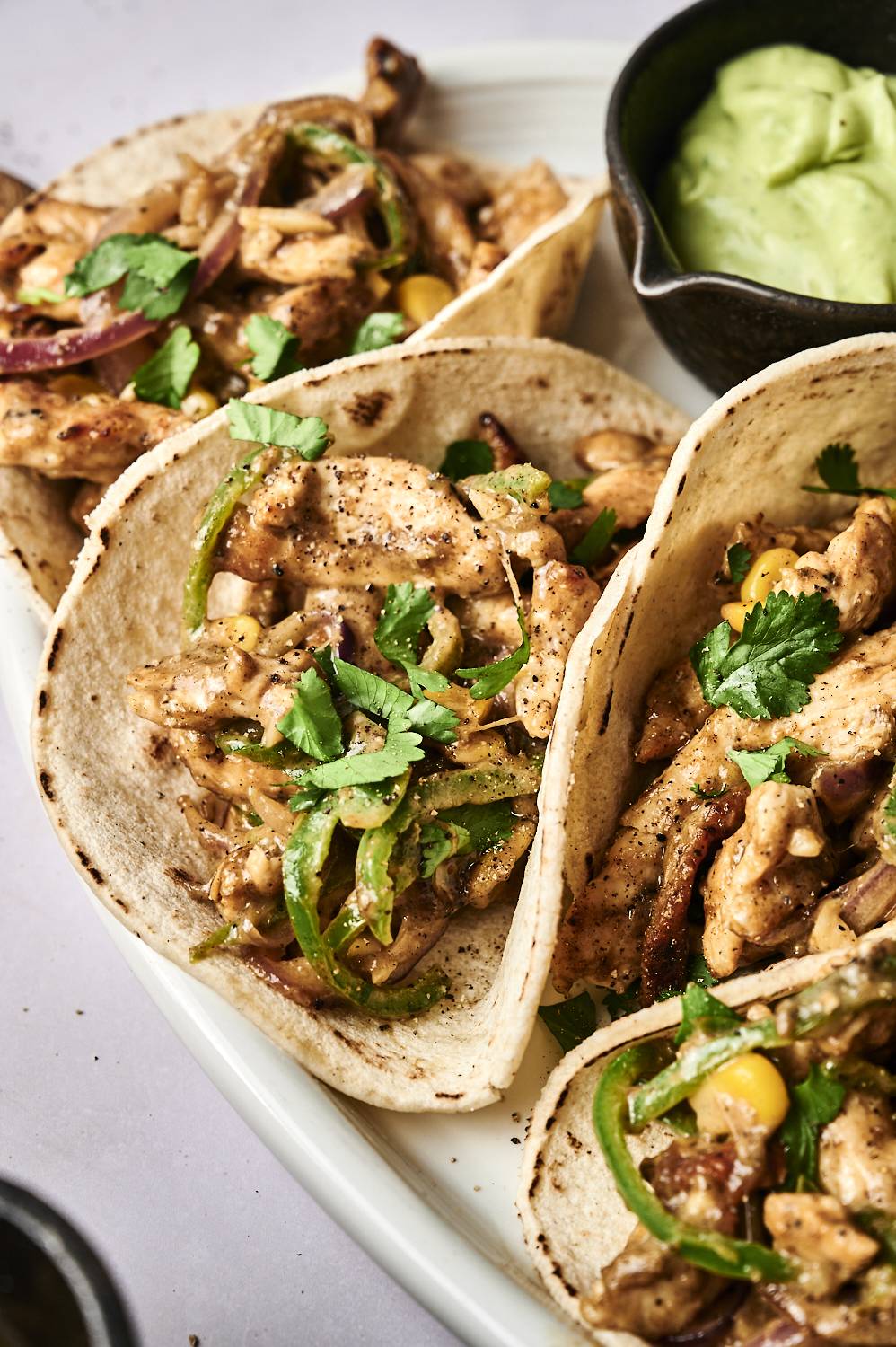 Three delicious tacos filled with grilled chicken, green peppers, and onions, garnished with fresh cilantro and served with guacamole.