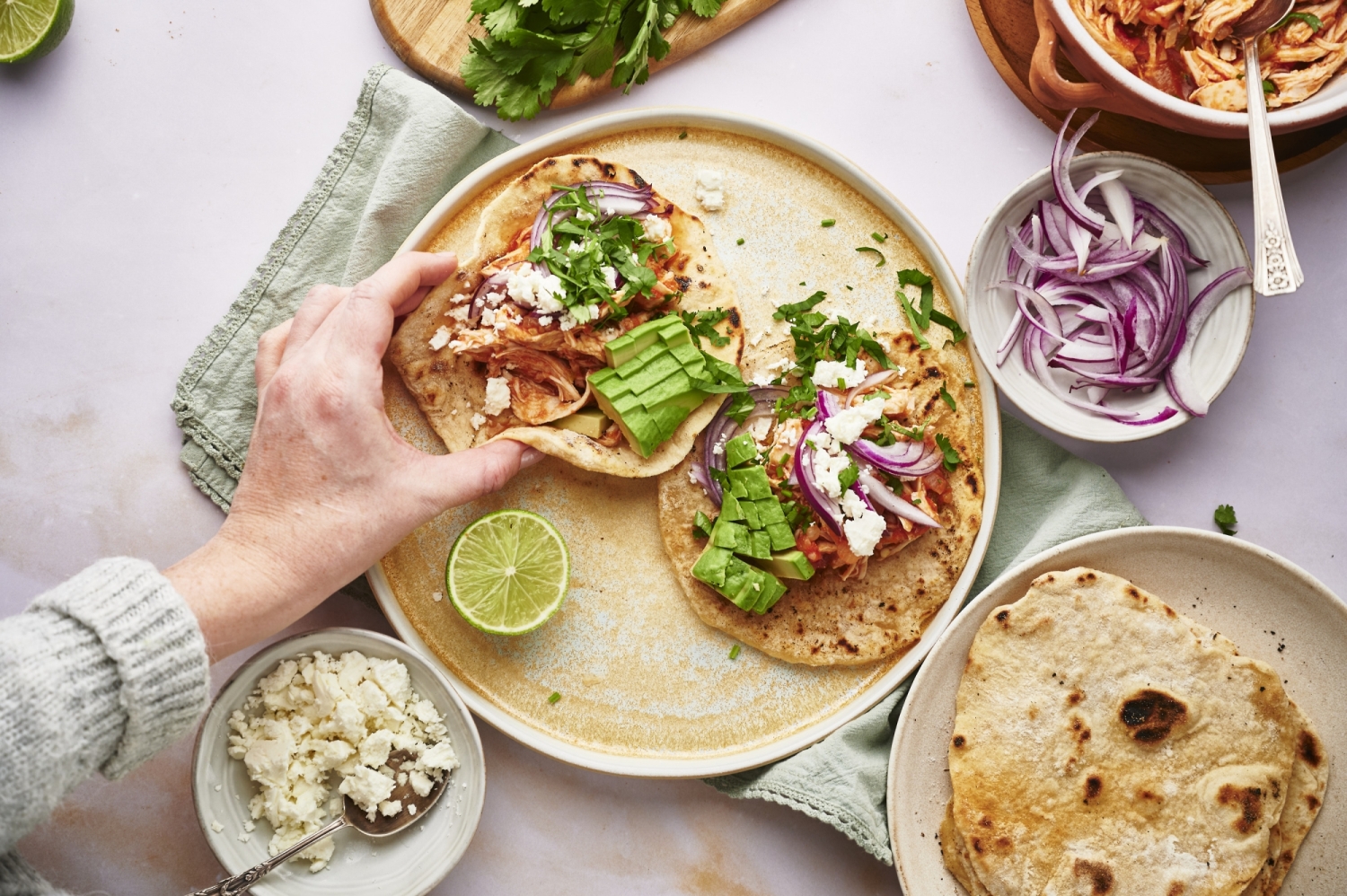 Tinga tacos with shredded chicken on corn tortillas served with queso fresco, red onion, cilantro, and avocado.