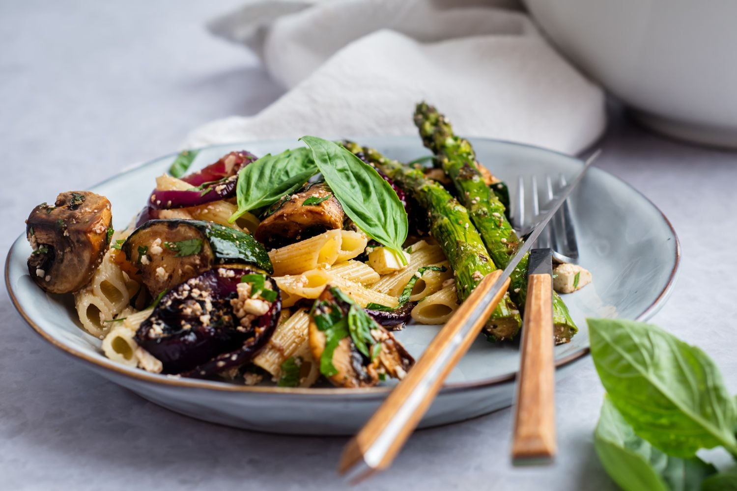 Pasta salad with grilled asparagus, zucchini, red onion, and mushrooms on a plate with feta cheese and balsamic vinaigrette.