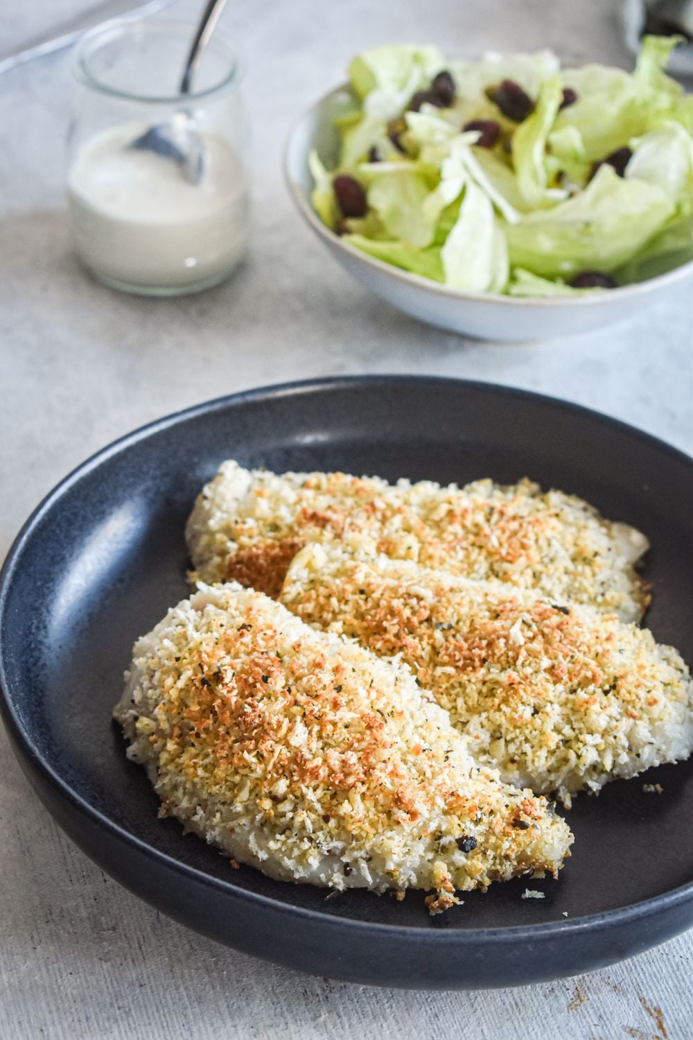Parmesan tilapia with Panko breadcrumbs and parmesan cheese on a plate with fresh herbs.
