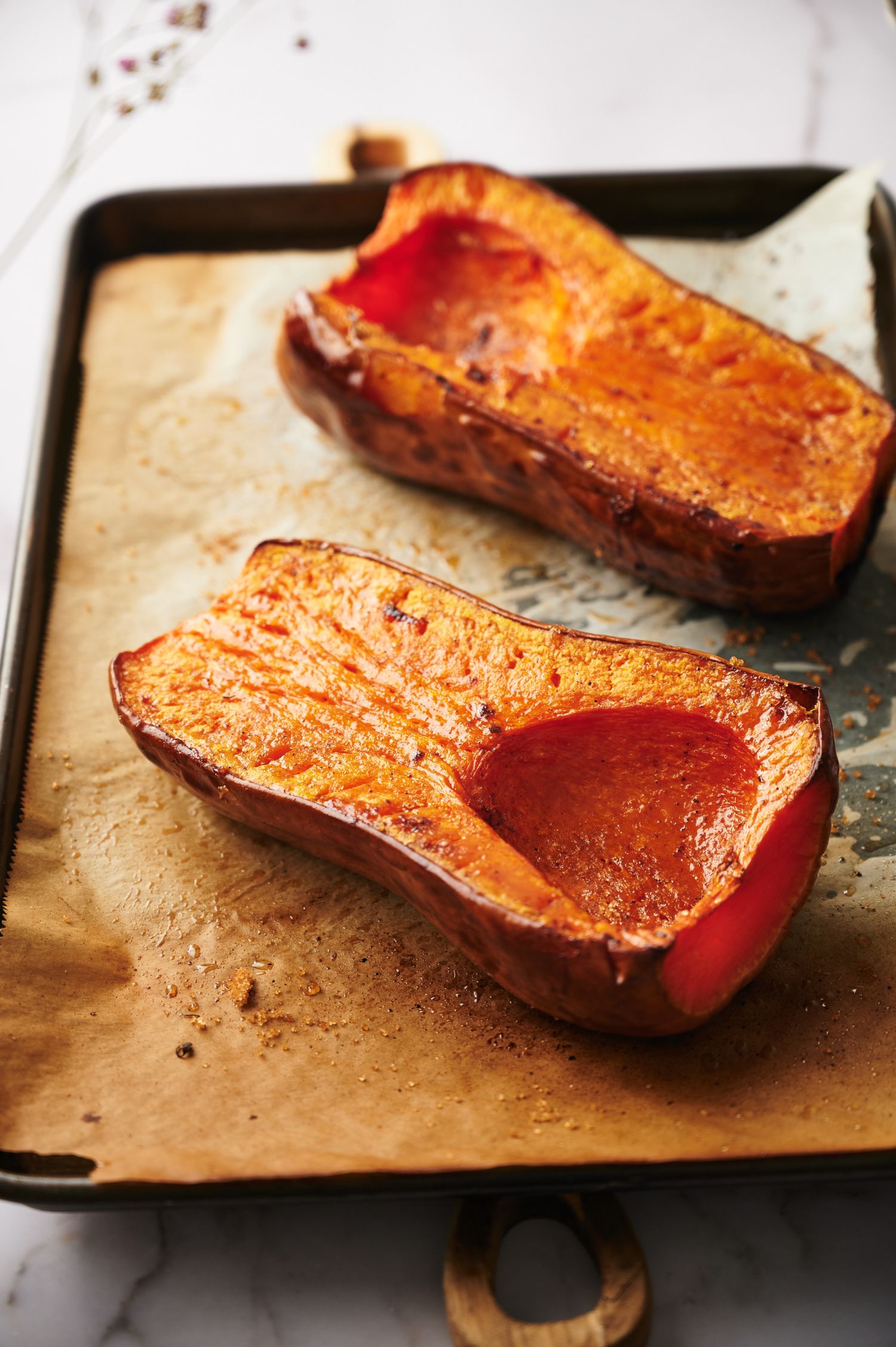 Whole butternut squash that is roasted on a baking sheet with parchment paper.