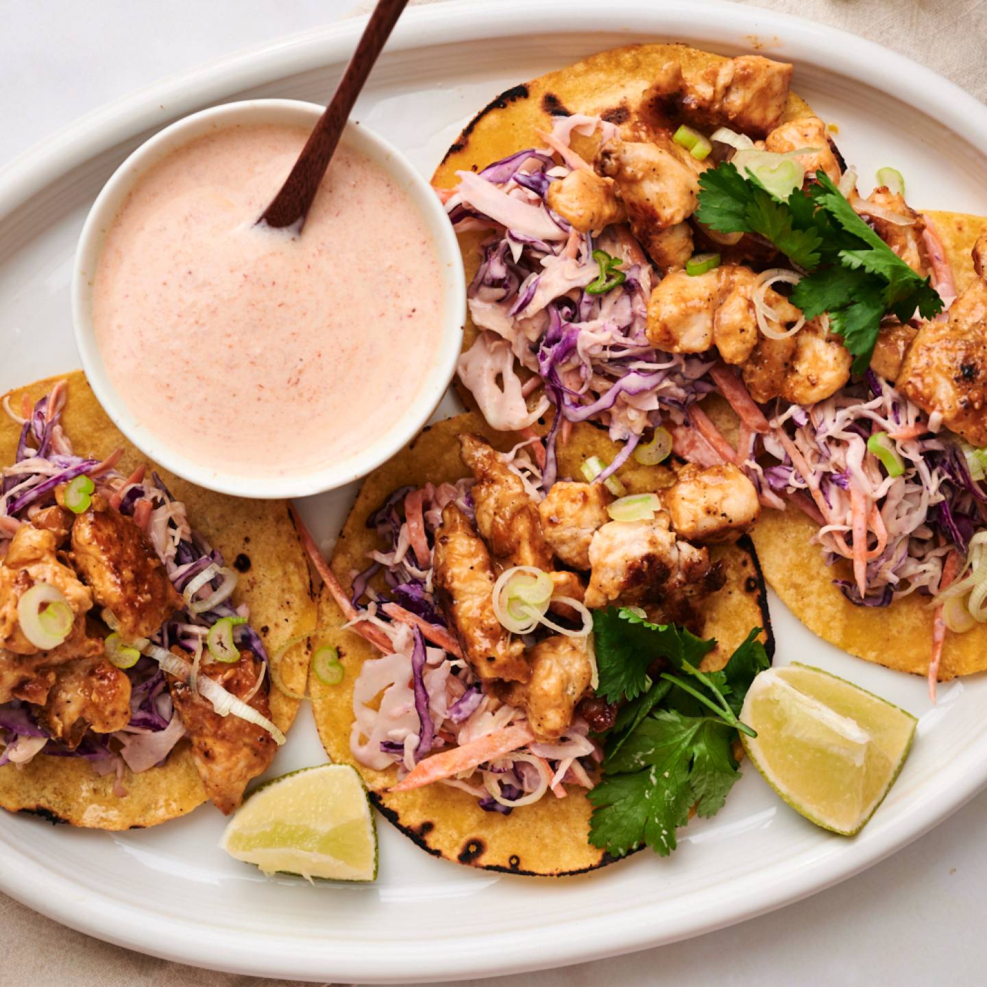 Bang bang chicken tacos served on warm corn tortilla with crunchy cabbage slaw, cilantro, lime wedges, and green onions.