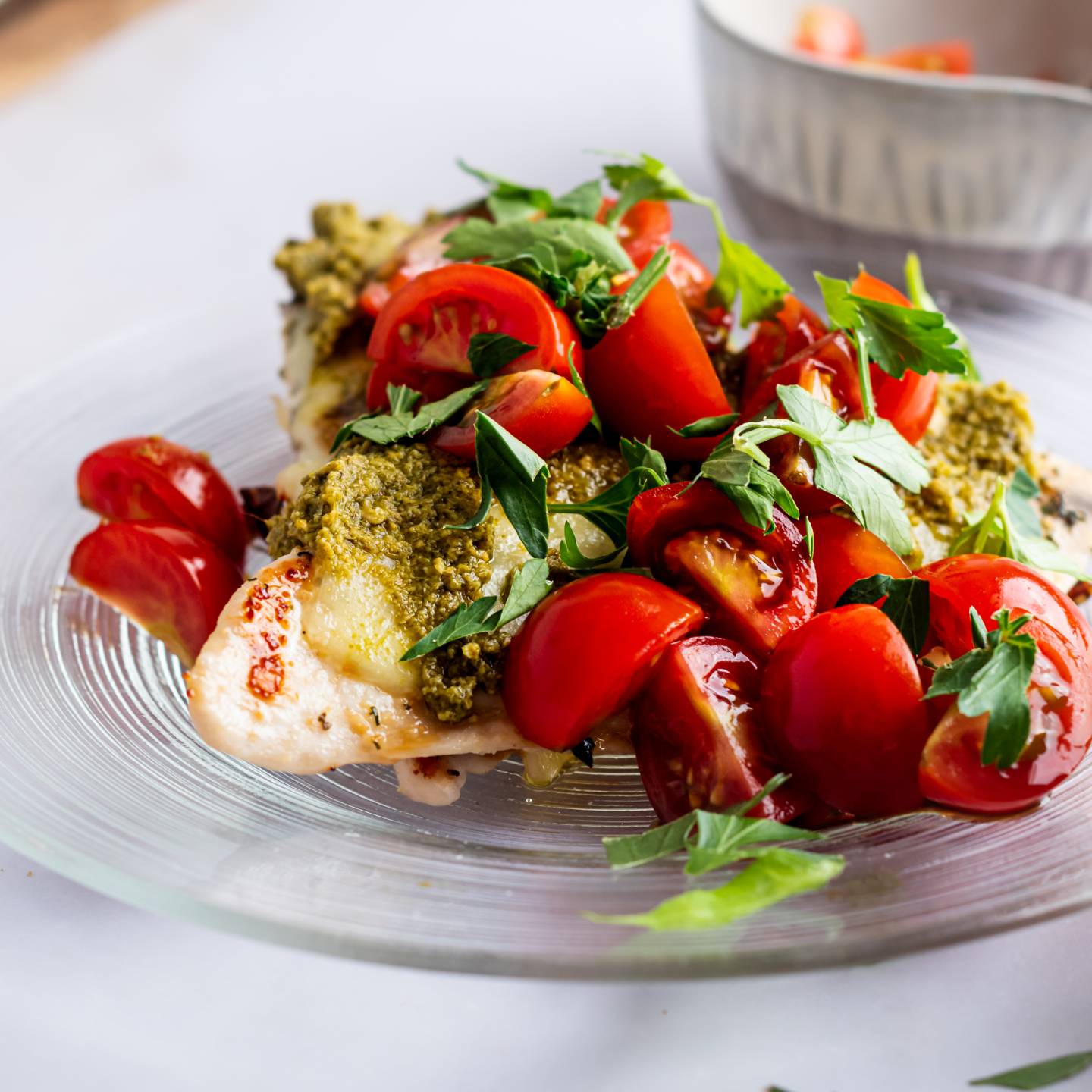 Grilled chicken margherita with cherry tomatoes, melted mozzarella cheese, and pesto on a plate.