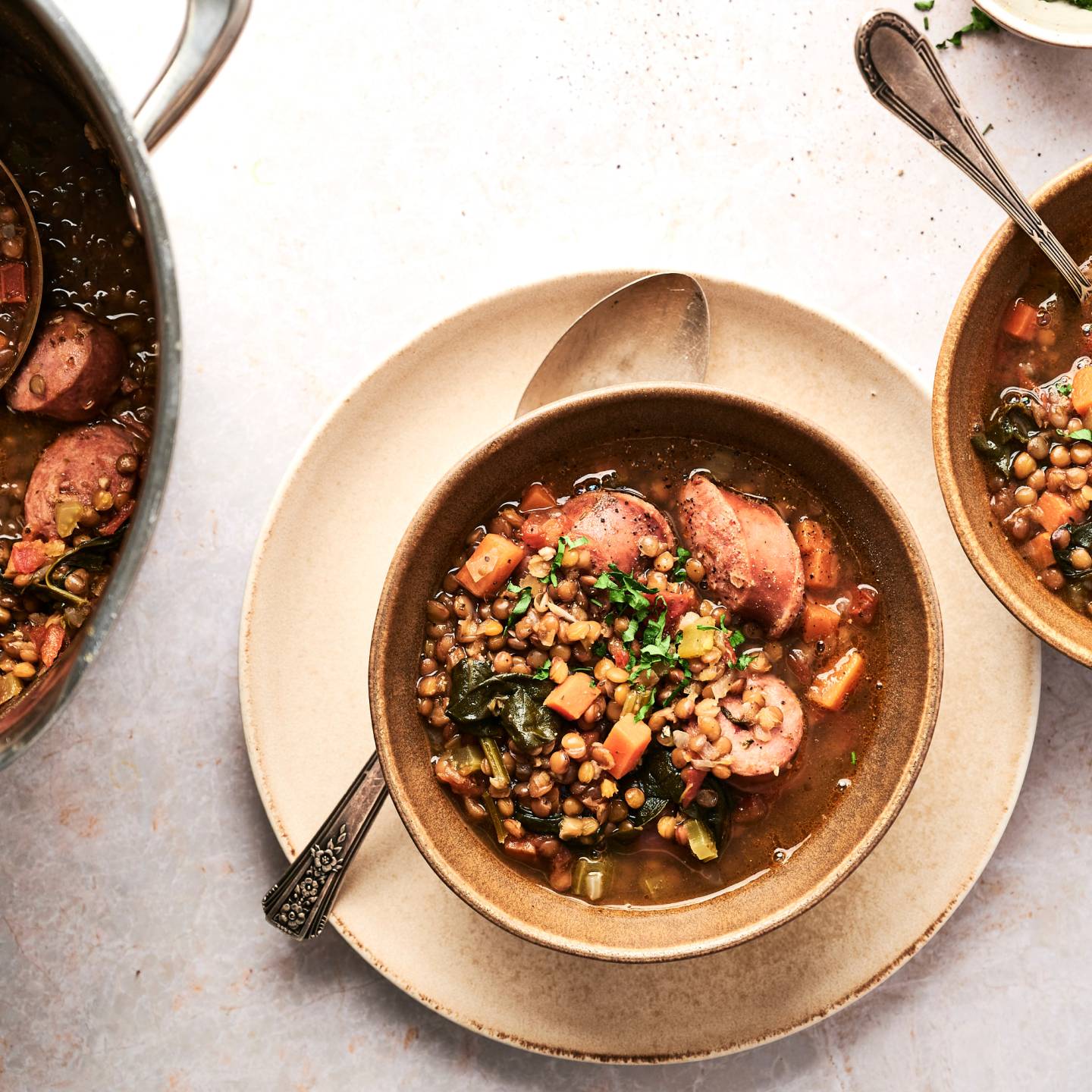 Sasuage, spinach, and lentils served in a tomato broth in two bowl and in a large soup pot.