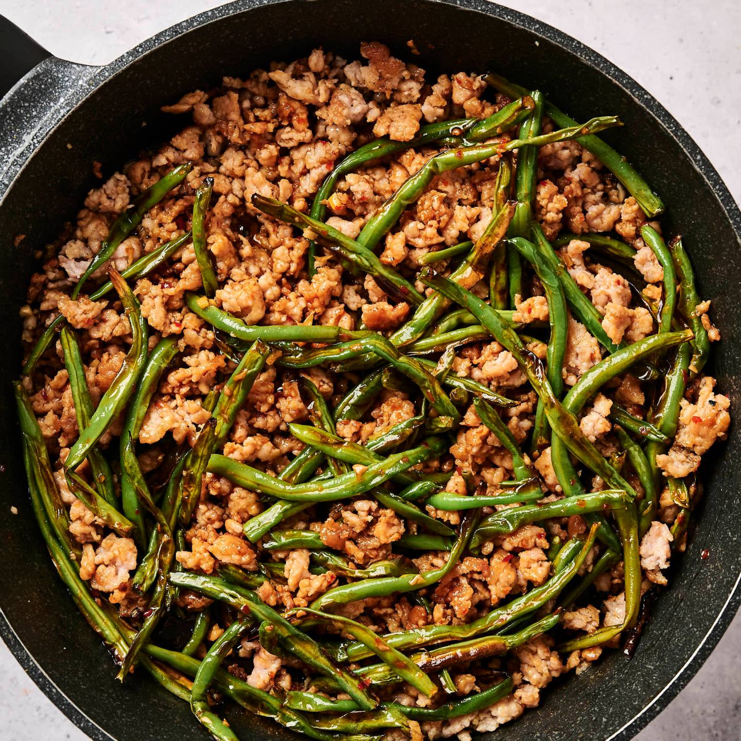 Ground turkey and green bean stir fry in a skillet with spicy sauce and chopsticks.