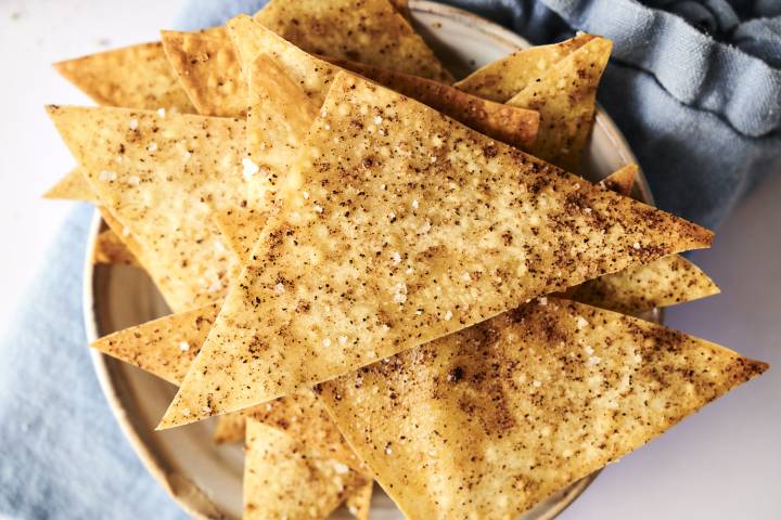 Golden baked wonton chips dusted with cinnamon sugar and sea salt on a plate with a blue napkin.