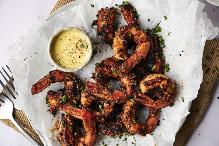 Grilled shrimp garnished with herbs, served with a creamy dipping sauce on parchment paper, ready to enjoy.