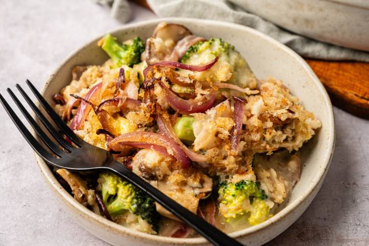A bowl of broccoli and mushroom casserole topped with crispy breadcrumbs and caramelized onions. A fork rests on the bowl, adding a cozy, inviting feel.