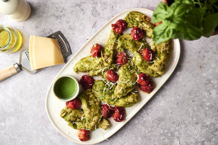 Juicy pesto chicken tenders topped with roasted cherry tomatoes and Parmesan cheese, served with extra pesto sauce on the side.