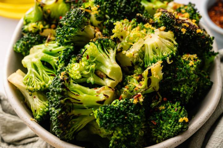 A bowl of roasted broccoli florets garnished with lemon zest and chili flakes. 