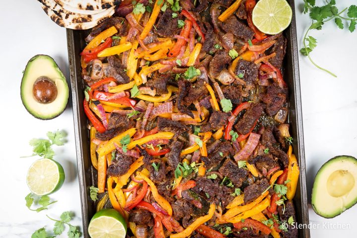 Sheet pan steak fajitas made with homemade fajita seasoning, flank steak, bell peppers, and onions on a sheet pan. 