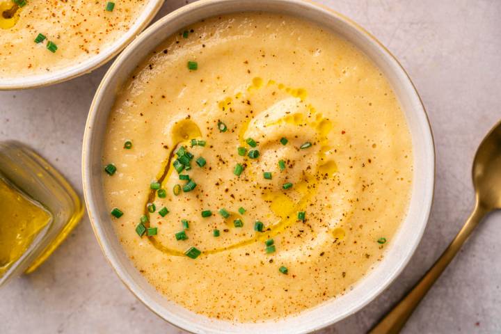 A creamy bowl of potato soup garnished with chopped chives and a drizzle of olive oil, with a sprinkle of black pepper. 