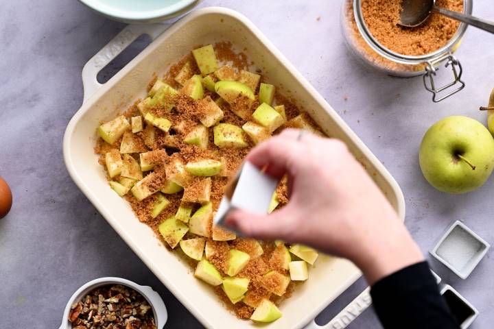 Chopped apples in a baking dish being sprinkled with brown sugar.