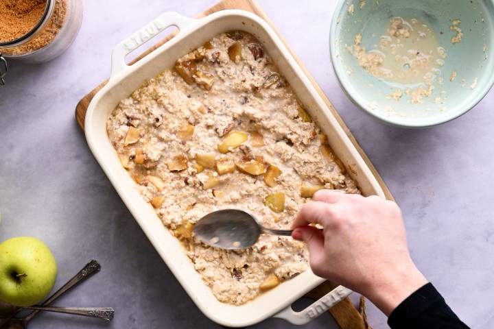 Oatmeal being stirred into a baking dish with apples.