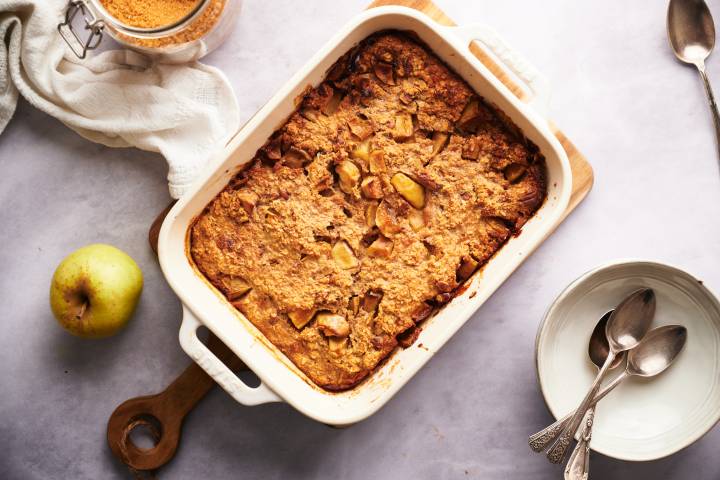 Baked apple oatmeal in a white baking dish with an apple on the side.