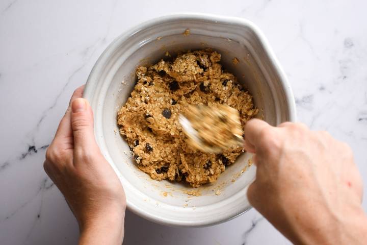 Mashed bananas, rolled oats, peanut butter, and chocolate chips being stirred in a bowl.
