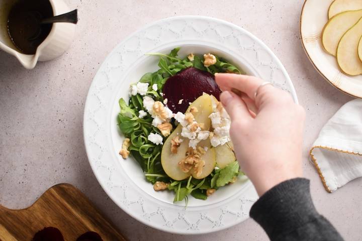 Goat cheese being sprinkled on a beet and arugula salad with pears.