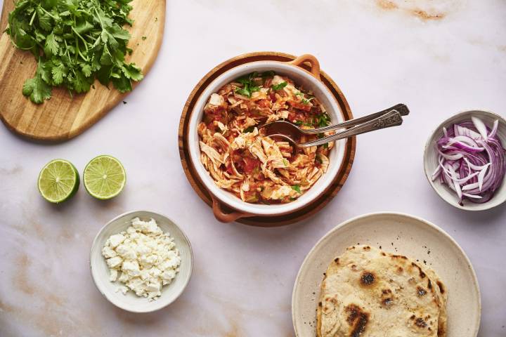 Chicken tinga in a bowl with tortillas and taco toppings on the side.