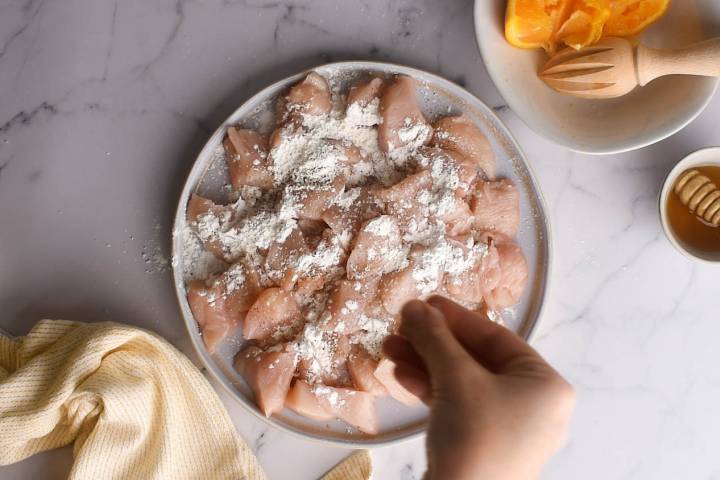 Chicken breast being coated with cornstarch, salt, and pepper.