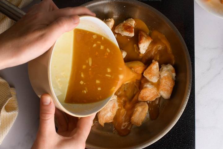 Orange sauce being added to a skillet with chicken breast.