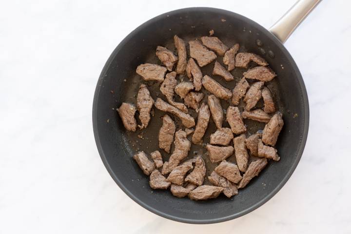 Flank steak cooking in a skillet.